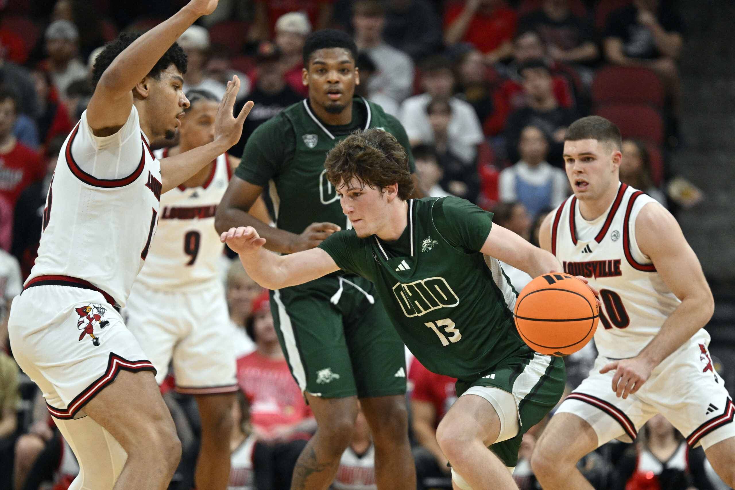 Nov 15, 2025; Louisville, Kentucky, USA;  Ohio Bobcats guard Jackson Paveletzke (13) dribbles against Louisville Cardinals forward Sananda Fru (13) during the second half at KFC Yum! Center. Louisville defeated Ohio 106-81. Mandatory Credit: Jamie Rhodes-Imagn Images