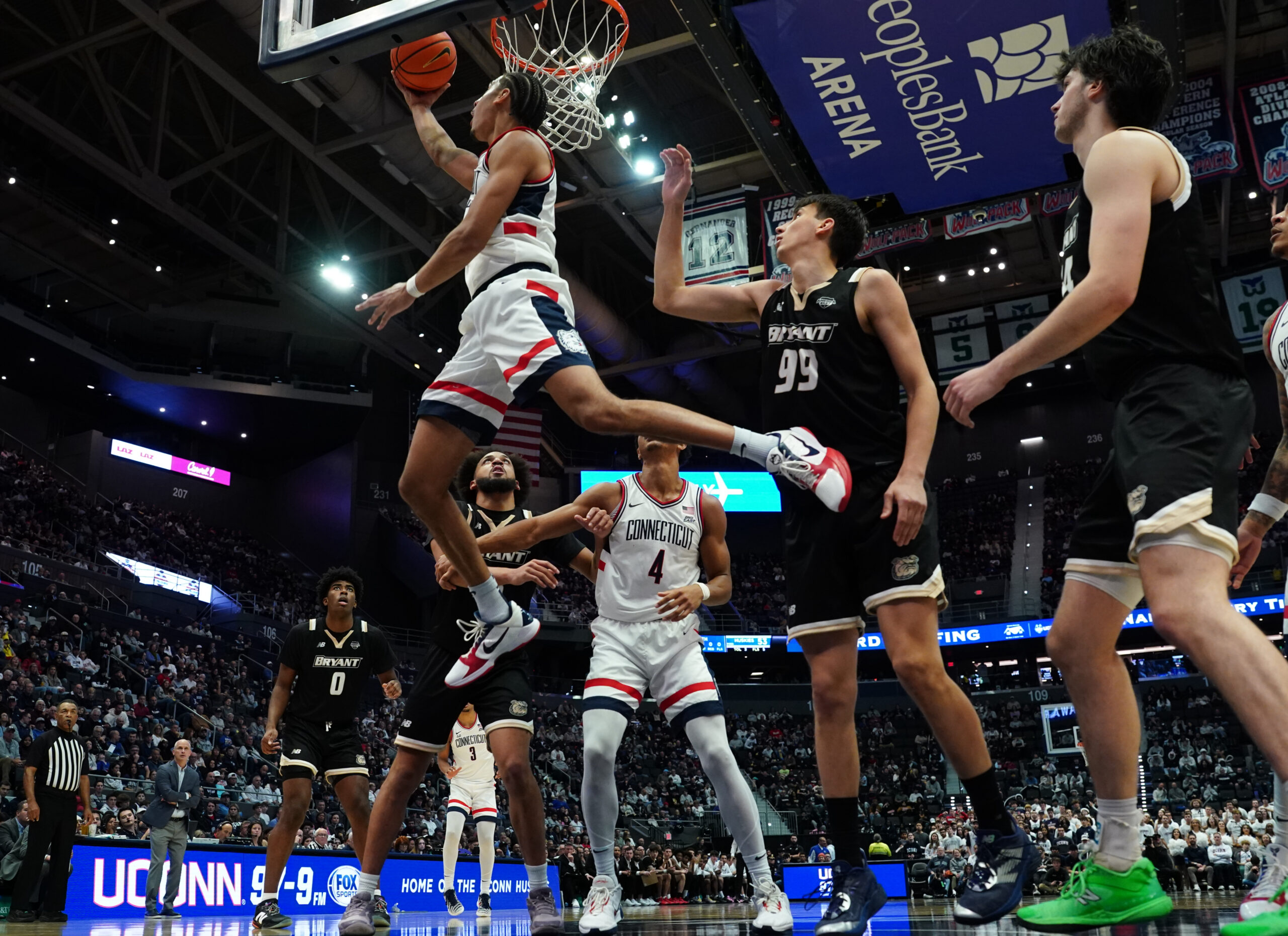 Nov 23, 2025; Hartford, Connecticut, USA; UConn Huskies forward Jayden Ross (23) makes the basket against Bryant Bulldogs guard Timofei Rudovskii (99) in the second half at Peoples Bank Arena. Mandatory Credit: David Butler II-Imagn Images