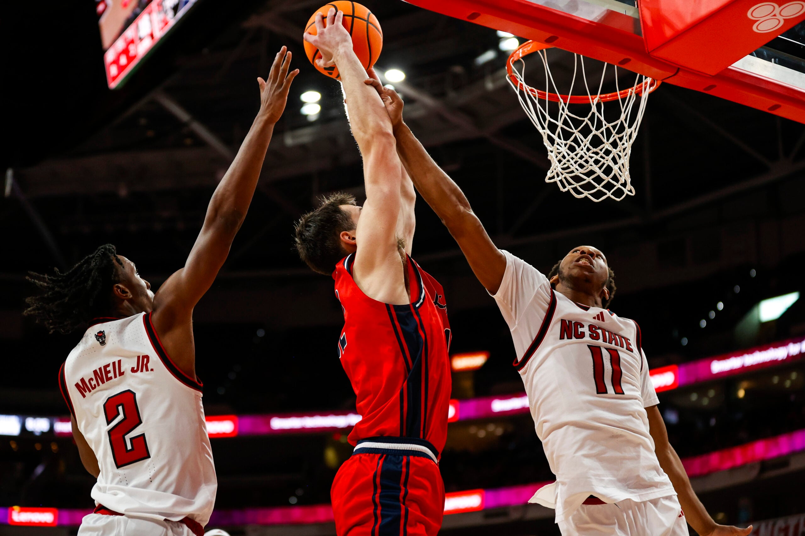 Dec 6, 2025; Raleigh, North Carolina, USA; Liberty Flames forward Josh Smith (12) attempts a dunk but is blocked by NC State Wolfpack guard Jr. Paul McNeil (2) and guard Quadir Copeland (11) during the second half of the game at Lenovo Center. Mandatory Credit: Jaylynn Nash-Imagn Images