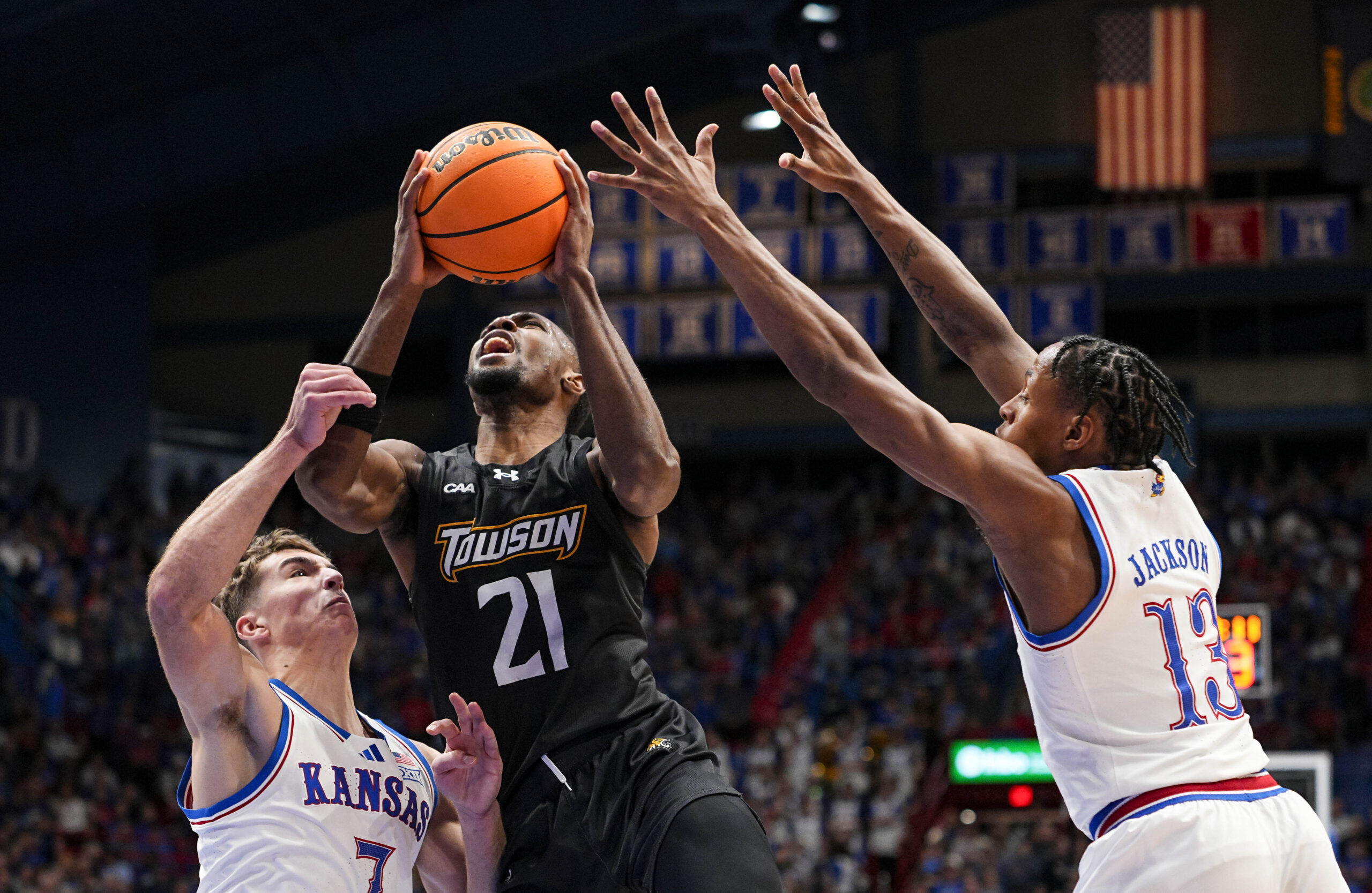 Dec 16, 2025; Lawrence, Kansas, USA; Towson Tigers guard Jack Doumbia Jr. (21) shoots against Kansas Jayhawks guard Kohl Rosario (7) and guard Elmarko Jackson (13) during the first half at Allen Fieldhouse. Mandatory Credit: Jay Biggerstaff-Imagn Images
