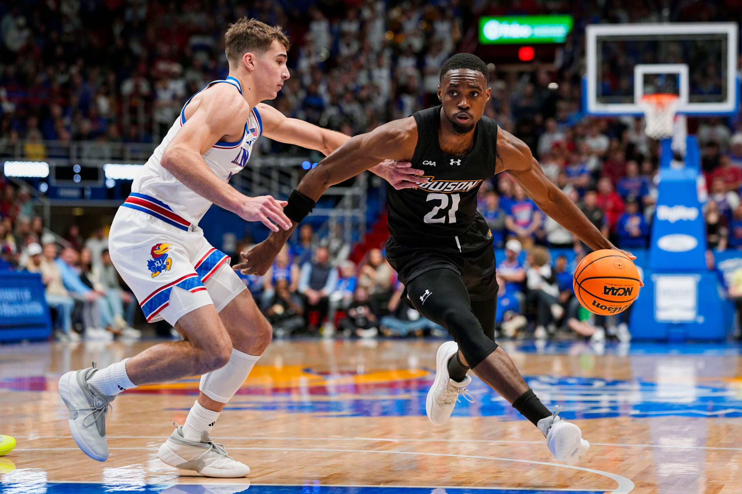 Dec 16, 2025; Lawrence, Kansas, USA; Towson Tigers guard Jack Doumbia Jr. (21) drives against Kansas Jayhawks guard Kohl Rosario (7) during the first half at Allen Fieldhouse. Mandatory Credit: Jay Biggerstaff-Imagn Images