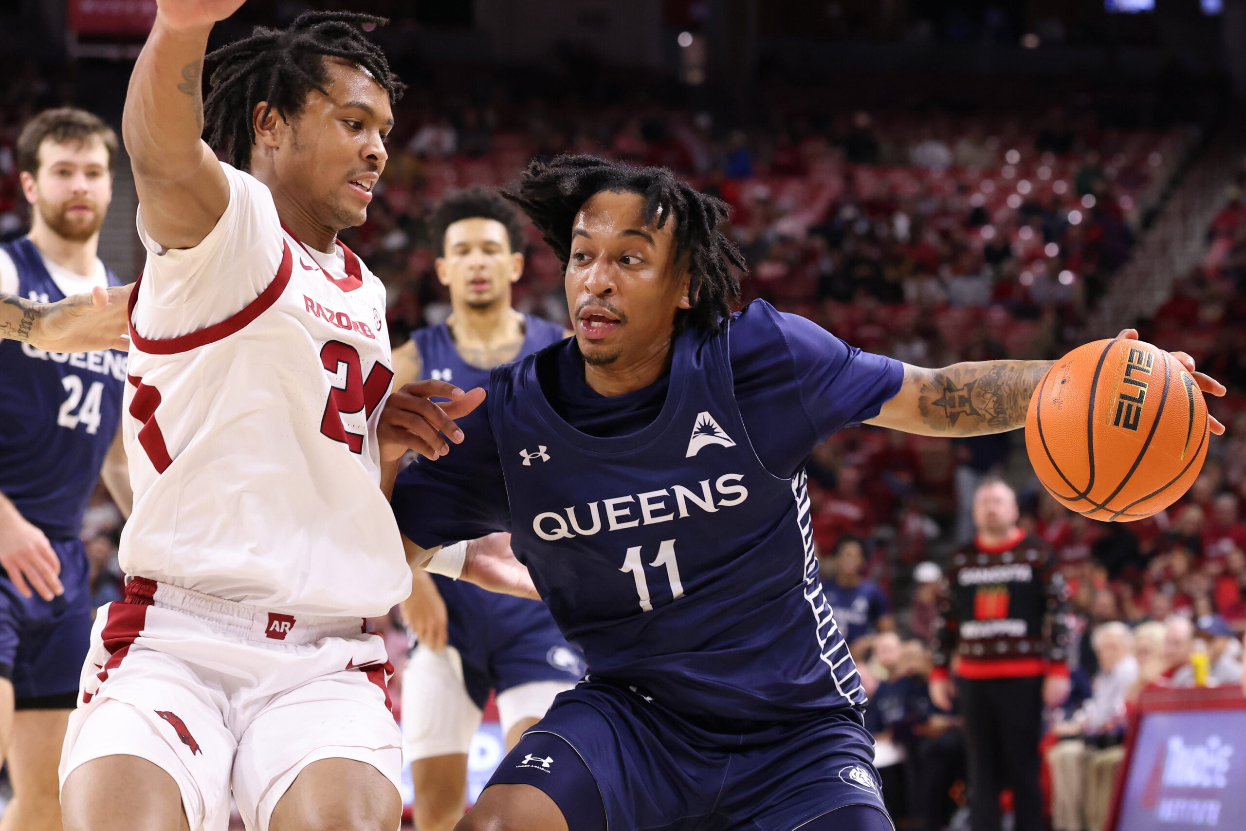 Dec 16, 2025; Fayetteville, Arkansas, USA; Queens Royals guard Chris Ashby (11) drives against Arkansas Razorbacks guard D.J. Wagner (21) during the first half at Bud Walton Arena. Mandatory Credit: Nelson Chenault-Imagn Images