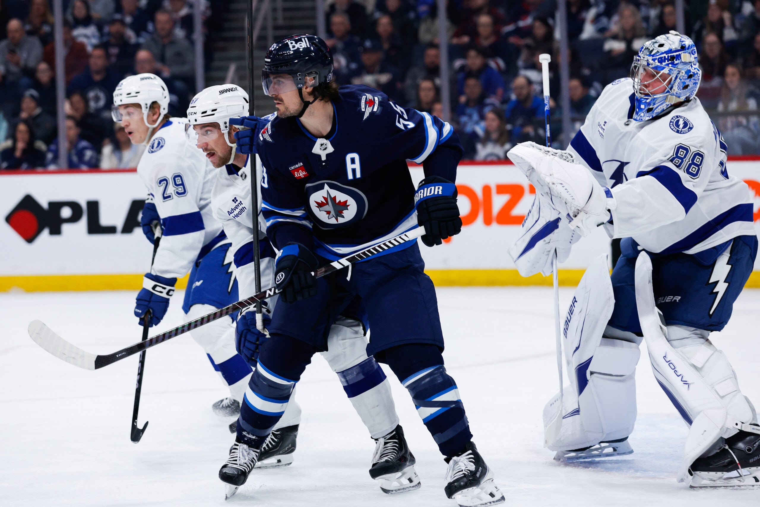 Mar 5, 2026; Winnipeg, Manitoba, CAN; Winnipeg Jets forward Mark Scheifele (55) jostles for position with Tampa Bay Lightning defenseman Charle-Edouard D'Astous (51) in front of goalie Andrei Vasilevsky (88) during the second period at Canada Life Centre. Mandatory Credit: Terrence Lee-Imagn Images