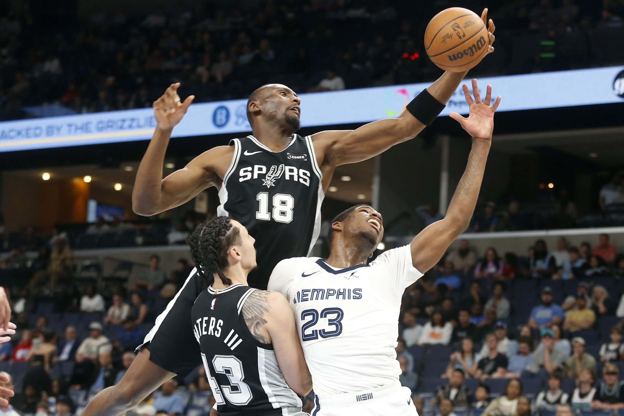 Mar 25, 2026; Memphis, Tennessee, USA; San Antonio Spurs center Bismack Biyombo (18) collects a rebound over forward Lindy Waters III (43) and Memphis Grizzlies forward Cedric Coward (23) during the fourth quarter at FedExForum. Mandatory Credit: Petre Thomas-Imagn Images