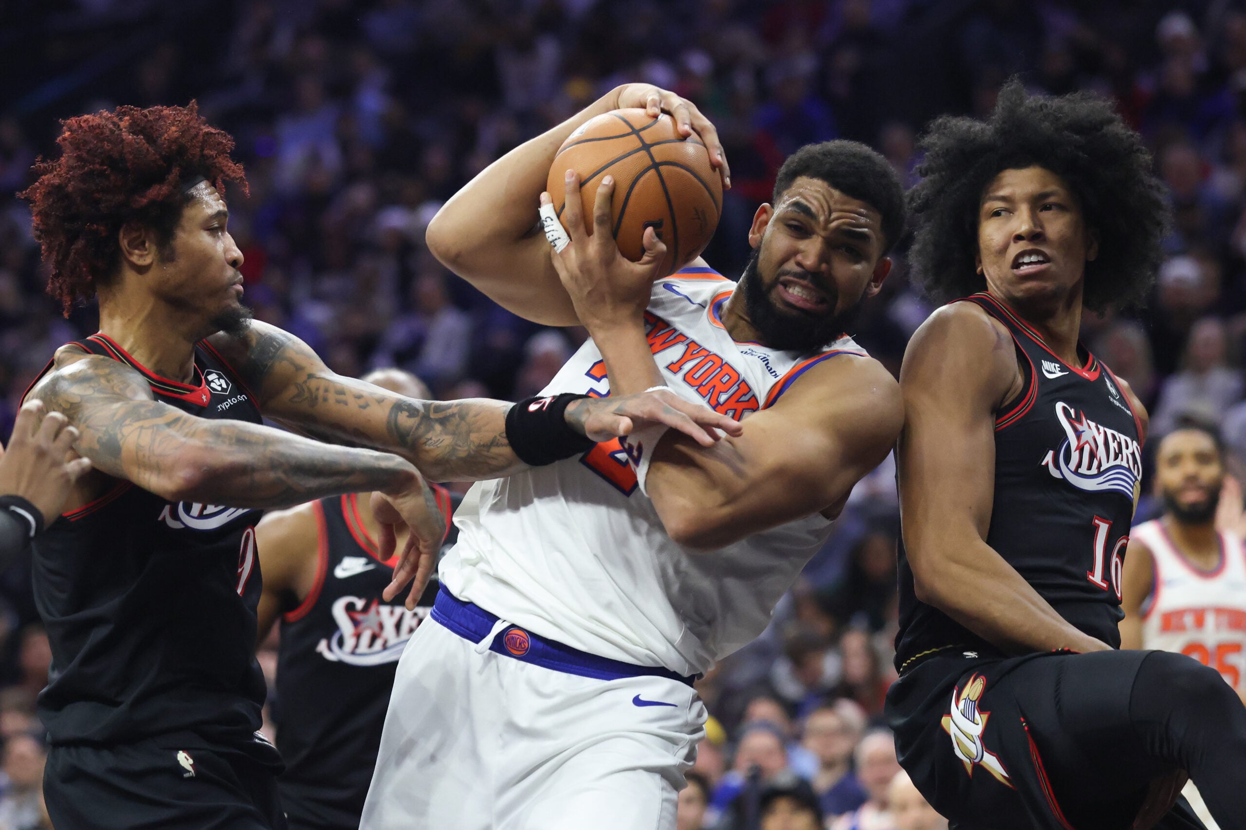 Feb 11, 2026; Philadelphia, Pennsylvania, USA; New York Knicks center Karl-Anthony Towns (32) drives against Philadelphia 76ers guard Kelly Oubre Jr. (9) and forward Marjon Beauchamp (16) during the first half at Xfinity Mobile Arena. Mandatory Credit: Bill Streicher-Imagn Images